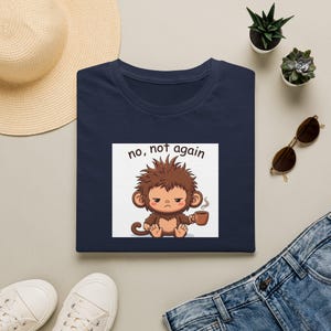 Könnte beinhalten: Ein marineblaues T-Shirt mit einer Grafik eines mürrischen, struppigen braunen Affen, der eine dampfende braune Kaffeetasse hält. Über dem Affen steht der Text "no, not again" in einer einfachen schwarzen Schrift. Das Motiv ist mittig platziert.