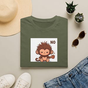 Könnte beinhalten: Ein olivgrünes T-Shirt mit einem Grafikdruck eines mürrischen Affen mit zerzaustem Haar, der eine kleine braune Kaffeetasse hält. Der Text NO ist in braunen Buchstaben neben dem Affen auf die Vorderseite des T-Shirts gedruckt.