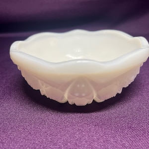 May include: A small, round, white milk glass bowl featuring a scalloped rim and a textured, embossed pattern along the exterior sides. The bowl has a smooth, glossy finish and a shallow, open basin design, showcasing a translucent quality.