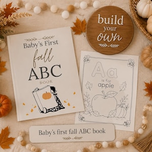 Puede incluir: Un libro Baby's First fall ABC con portada blanca y una ilustración de calabaza, una página para colorear a juego con una manzana y un letrero redondo de madera con el texto build your own, rodeados de pequeñas calabazas y hojas.