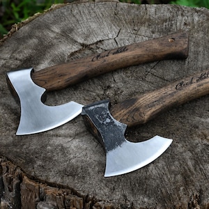 Könnte beinhalten: Zwei Äxte mit Holzgriffen und silbernen Klingen liegen auf einem Baumstumpf. Die Griffe sind mit den Worten "Cloud whale" graviert. Die Klingen haben ein gebogenes Design.