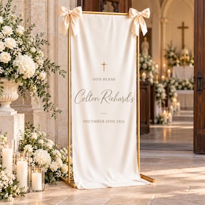 Puede incluir: Una pancarta de tela color crema, alta y rectangular, suspendida de un marco de metal dorado con lazos color crema en las esquinas superiores. La pancarta presenta una cruz dorada y el texto "GOD BLESS", "Colton Richard's" y "DECEMBER 20TH 2026".
