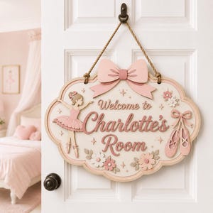Op de afbeelding: Een decoratief houten deurbord met een ballerina-illustratie, balletschoenen en bloemaccenten in roze en crèmetinten. Het bord toont de tekst Welcome to Charlotte's Room in script, bekroond met een grote roze strik en een touw om op te hangen.
