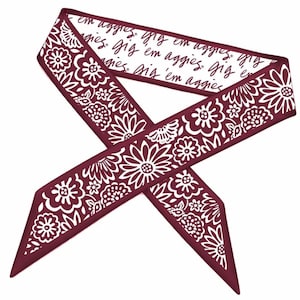 Könnte beinhalten: Ein weinroter und weißer Schal mit floralem Muster und dem Text "Gig 'em aggies" auf weißem Hintergrund. Der Schal hat ein Blumendesign an den Rändern.