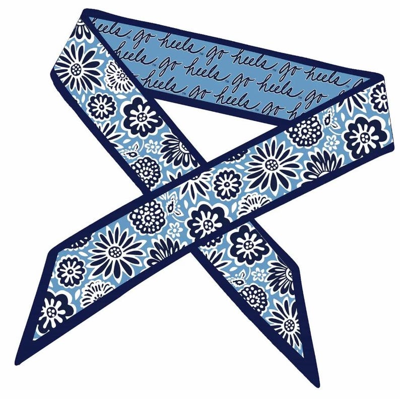 Op de afbeelding: Een lange, smalle sjaal met een lichtblauwe achtergrond en een herhalend donkerblauw en wit bloemenpatroon. E&eacute;n kant toont de herhaalde cursieve tekst "go heels" in het donkerblauw, terwijl de andere kant een dicht bloemenmotief heeft.