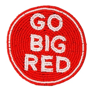May include: A circular coaster crafted from small red and white beads. The design features the text GO BIG RED in white beads against a solid red background, with a white beaded border encircling the entire edge of the round beaded coaster.