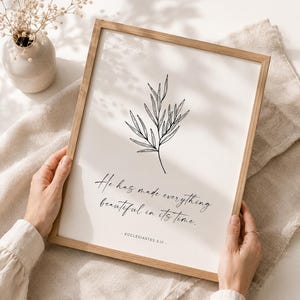 Puede incluir: Un marco de madera rectangular que contiene una impresión blanca con un dibujo de línea negra de una rama con hojas. El texto dice: He has made everything beautiful in its time. - ECCLESIASTES 3:11. La impresión está en un marco de madera clara.