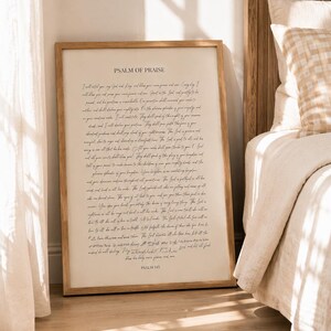 Può includere: Una stampa rettangolare incorniciata che presenta il testo Psalm of Praise e Psalm 145 con un lungo passaggio in scrittura corsiva con inchiostro nero su uno sfondo color crema. La cornice è in legno chiaro con un design semplice e pulito.