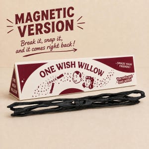 May include: A black, textured, branch-like object with a magnetic center, positioned in front of a triangular cardboard box. The box features the text "MAGNETIC VERSION," "Break it, snap it, and it comes right back!," "ONE WISH WILLOW," and "You only get ONE WISH."