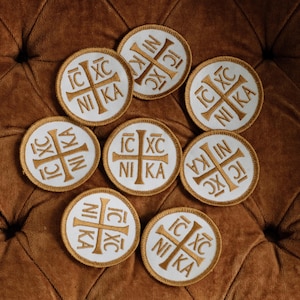 May include: Eight circular embroidered patches featuring a white background with a gold cross and the Greek letters IC XC NI KA arranged in the four quadrants. Each patch has a gold stitched border and a clean, circular design.