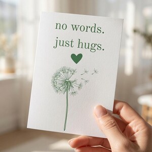 May include: A white rectangular greeting card featuring the green text "no words. just hugs." above a small green heart and a line-art illustration of a dandelion with seeds blowing to the right in a soft green ink on a textured paper.