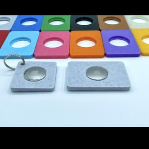 May include: A collection of colorful square keychains with a circular hole in the center. Two gray keychains with a silver Apple logo are in the foreground. The keychains are in various colors, including blue, green, pink, orange, and purple.