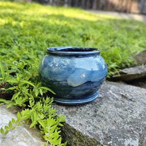 May include: A round ceramic planter with a glossy finish featuring a gradient of deep navy blue at the base transitioning into a lighter, sky blue hue toward the rim. The vessel has a wide, circular opening and a distinct, raised circular base.