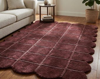 May include: A rectangular area rug in a deep burgundy color featuring a grid pattern of raised squares. The rug has a distinct scalloped edge design along its entire perimeter, creating a soft, rounded border effect on the floor surface.