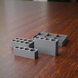 May include: A set of three grey organizers with a ribbed texture. One rectangular piece features eight circular openings, another is a taller rectangular block with four circular openings, and the third is a shallow tray with six rectangular compartments.