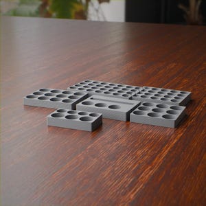 May include: A set of modular gray storage organizers featuring multiple circular cutouts for holding small items. The collection includes various rectangular blocks with different hole configurations and a central piece with a horizontal slot.