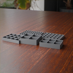 May include: A set of four gray plastic storage organizers with various grid configurations. The collection includes one central square container with four compartments, flanked by three rectangular trays featuring smaller square dividers.