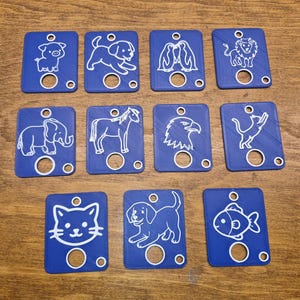 May include: A collection of blue rectangular tags, each featuring a white outline of a different animal: pig, dog, penguins, lion, elephant, horse, eagle, cat, cat, dog, and fish. Each tag has a central hole and two smaller holes.