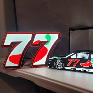 May include: A pair of illuminated signs featuring the number 77 in a bold white font with red accents. One sign is a standalone number 77, while the other is a race car silhouette labeled with the number 77, a red chili pepper, and text.