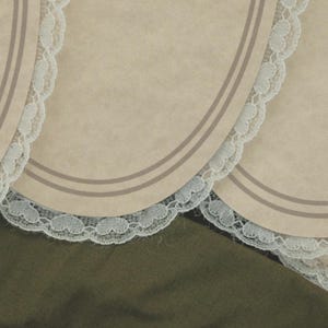 May include: Close-up of several beige placemats with a scalloped white lace trim. Each placemat has two thin, parallel gray lines near the edge. The background is a dark olive green fabric.