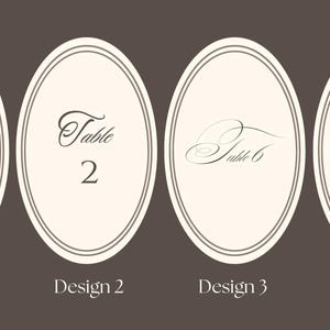 May include: Four oval table number cards with a cream background and a brown border. The cards feature the words "Table 2" and "Table 6" in elegant script. The bottom of the cards read "Design 1", "Design 2", "Design 3", and "Design 4".
