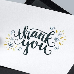 May include: A white rectangular greeting card featuring the dark blue cursive text thank you, surrounded by small blue flower illustrations and gold leaf accents, partially inserted into a solid black envelope with a pointed flap.