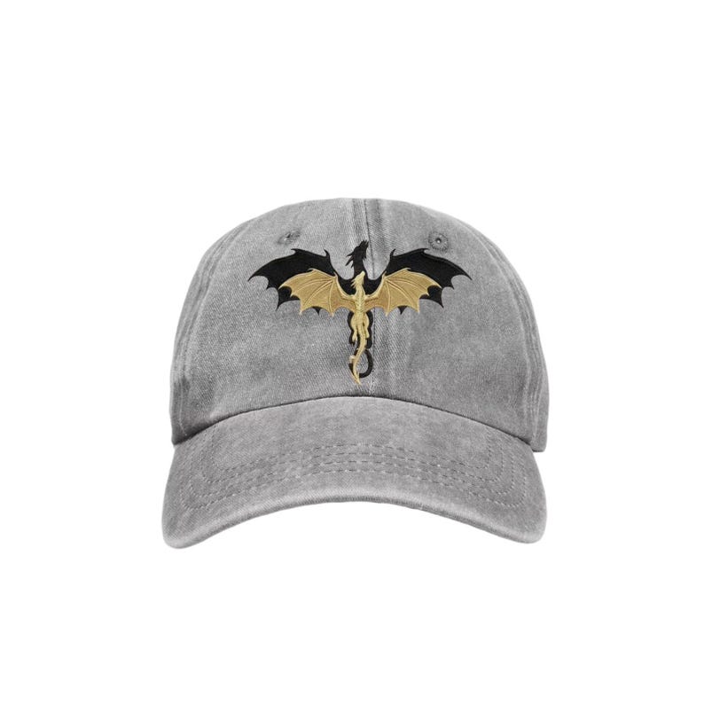 May include: A gray baseball cap featuring a gold and black dragon design. The dragon is embroidered on the front of the cap, with its wings spread wide. The cap has a curved brim and an adjustable strap.