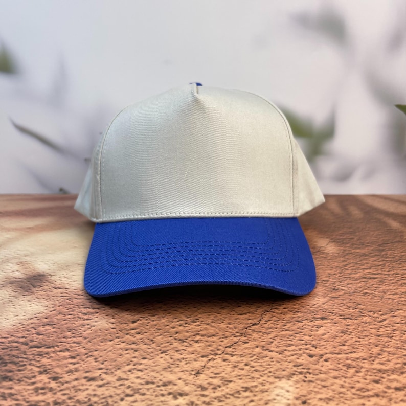 May include: A baseball cap with a light gray crown and a royal blue brim. The cap is made of a sturdy fabric and has a classic, structured design. The brim is curved and stitched.