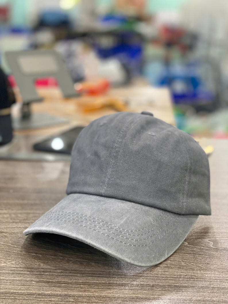 May include: A gray baseball cap with a curved brim. The cap is made of a soft fabric and has a classic, unstructured design. The brim features a row of stitching.