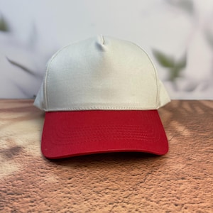 May include: A baseball cap with a white crown and a red brim. The cap is made of a sturdy fabric and has a classic, structured design. The color combination is bold and eye-catching, suitable for casual wear.