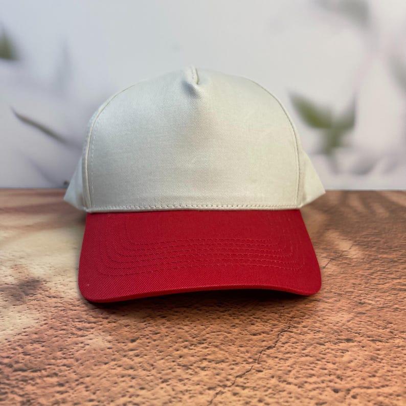May include: A baseball cap with a white crown and a red brim. The cap is made of a sturdy fabric and has a classic, structured design. The color combination is bold and eye-catching, suitable for casual wear.