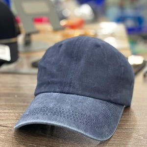 May include: A navy blue baseball cap with a pre-curved brim. The cap has a faded, vintage look, with a slightly lighter shade of blue on the brim. The crown is a solid color, and the cap appears to be made of a soft, worn fabric.
