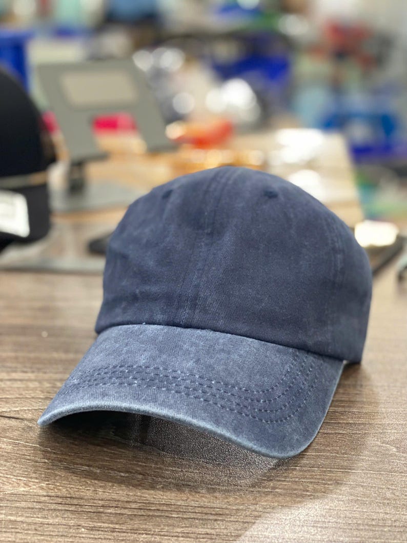 May include: A navy blue baseball cap with a pre-curved brim. The cap has a faded, vintage look, with a slightly lighter shade of blue on the brim. The crown is a solid color, and the cap appears to be made of a soft, worn fabric.