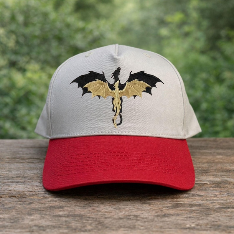 May include: A baseball cap with a red brim and a light gray crown. The cap features an embroidered dragon design with black and gold wings. The dragon is centered on the front of the cap, creating a striking visual.