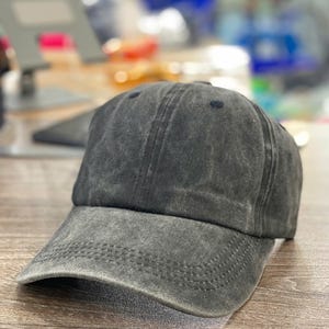 May include: A charcoal gray baseball cap with a curved brim. The cap has a distressed, faded appearance and a six-panel design. The hat is made of a soft, textured fabric and features a stitched brim.