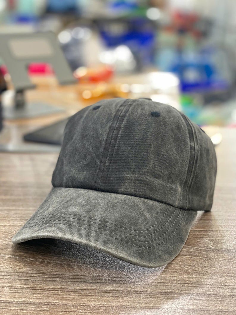 May include: A charcoal gray baseball cap with a curved brim. The cap has a distressed, faded appearance and a six-panel design. The hat is made of a soft, textured fabric and features a stitched brim.