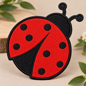 May include: A circular embroidered patch featuring a ladybug design. The ladybug has a bright red body with black circular spots, a black head, and two black antennae extending from the top. The entire design is outlined in black thread.