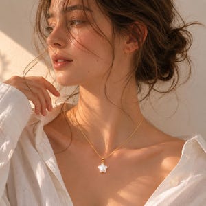 May include: A gold-toned chain necklace featuring a single white star-shaped pendant. The pendant has a smooth, pearlescent finish and is suspended from a delicate, thin metal chain that rests against the collarbone area of the wearer.