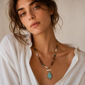 May include: A necklace featuring a large, irregular turquoise pendant suspended from a strand of mixed beads. The strand includes white freshwater pearls, small metallic gold-toned spacers, and round brown and teal-coloured stone beads.