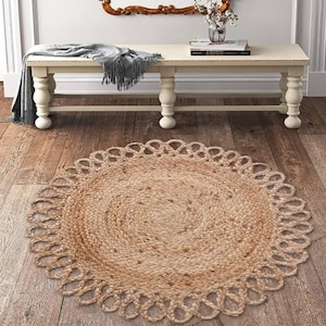 Può includere: Un tappeto rotondo in iuta naturale con un bordo smerlato decorativo. Il tappeto è di colore marrone chiaro ed è posizionato su un pavimento in legno. Il design del tappeto presenta un motivo a spirale al centro.