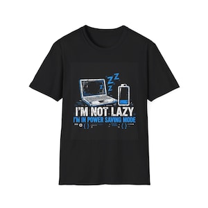 May include: A black short-sleeved t-shirt featuring a graphic of a laptop and a battery icon with blue Zs. The text reads I'M NOT LAZY I'M IN POWER SAVING MODE, accompanied by small code bracket symbols and gear icons in white and blue ink.