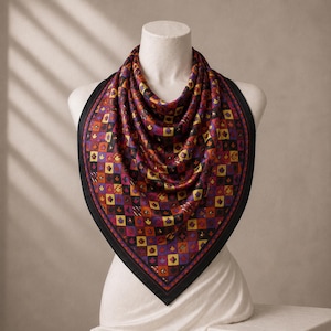 May include: A square silk scarf featuring a repeating grid pattern of small maple leaves in shades of orange, yellow, purple, and red. The scarf has a solid black border and is draped over a mannequin, displaying a vibrant, multi-coloured autumn-inspired design.