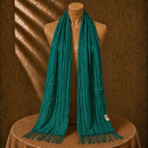 May include: A long, rectangular teal scarf with a crinkled, textured surface and subtle metallic shimmer. The scarf features vertical pleats running the length of the fabric and is finished with delicate, matching fringe at both ends.