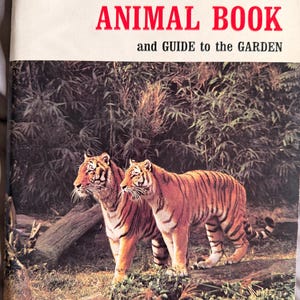 May include: A book titled PHILADELPHIA ZOO ANIMAL BOOK and GUIDE to the GARDEN. The cover features a photograph of two orange and black striped tigers standing in a dense, green, leafy forest environment with a fallen log in the foreground.