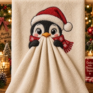 Può includere: Un asciugamano testurizzato color crema con un pinguino ricamato che indossa un cappello da Babbo Natale rosso e una sciarpa rossa abbinata con motivi a fiocchi di neve bianchi. Il pinguino ha un piumaggio bianco e nero, occhi grandi e un becco arancione.