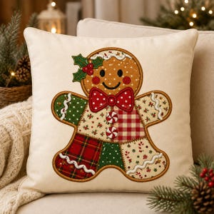 Peut inclure: Un coussin carré blanc cassé avec une applique centrale en forme de bonhomme en pain d'épices. Le personnage est orné d'un nœud papillon rouge à pois, de deux bonbons à la menthe et d'un brin de houx. Le corps est fait de tissus variés.