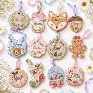 May include: A collection of twelve embroidered felt ornaments featuring various shapes including a mushroom, fox, bear, gingerbread person, stocking, and snow globe. Each ornament is personalized with names like Hazel, Rowan, Finn, Ivy, Theo, Clara, Jack, Mia, Noel, Holly, and Ella, and includes a satin ribbon loop for hanging.