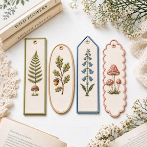 May include: Four fabric bookmarks with embroidered botanical designs. One rectangular with a fern and mushroom, one oval with an oak branch and acorn, one pointed with blue bellflowers, and one scalloped with three mushrooms, each with a metal eyelet.
