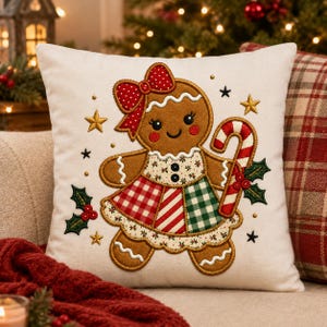 Può includere: Un cuscino quadrato color bianco sporco con il ricamo di un omino di pan di zenzero che indossa un fiocco rosso a pois bianchi, un vestito a quadri rossi e verdi, e tiene in mano un bastoncino di zucchero a righe rosse e bianche.