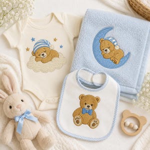 May include: A cream-colored short-sleeve bodysuit with an embroidered bear sleeping on a cloud, a light blue fleece blanket with a bear sleeping on a crescent moon, a white bib with a bear wearing a blue bow tie, and a plush rabbit toy.